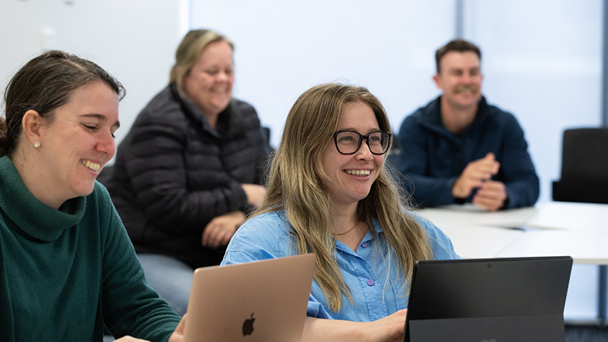 Three women seated at a table, each using a laptop, engaged in discussion and collaboration.
