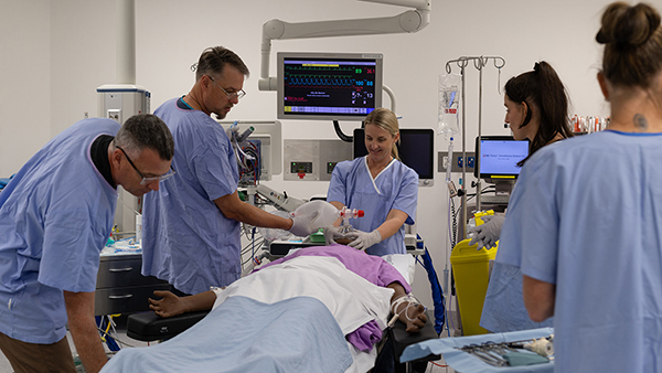 Group of medical professionals examining a patient mannequin in a hospital setting.