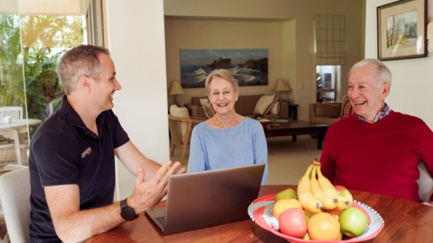 A group of three people gathered around a table with a laptop open in front of them.