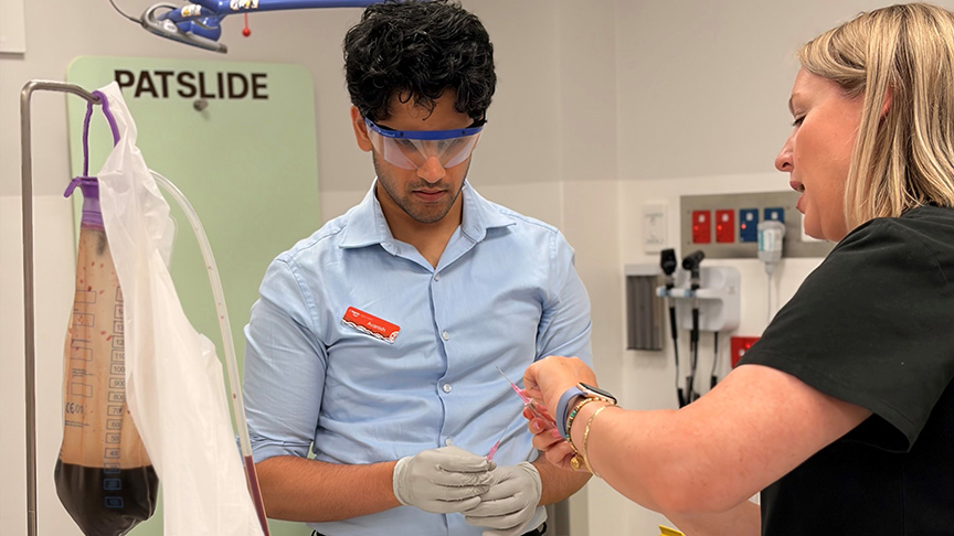 A woman dressed in a black shirt teaching medical procedure to a male student.