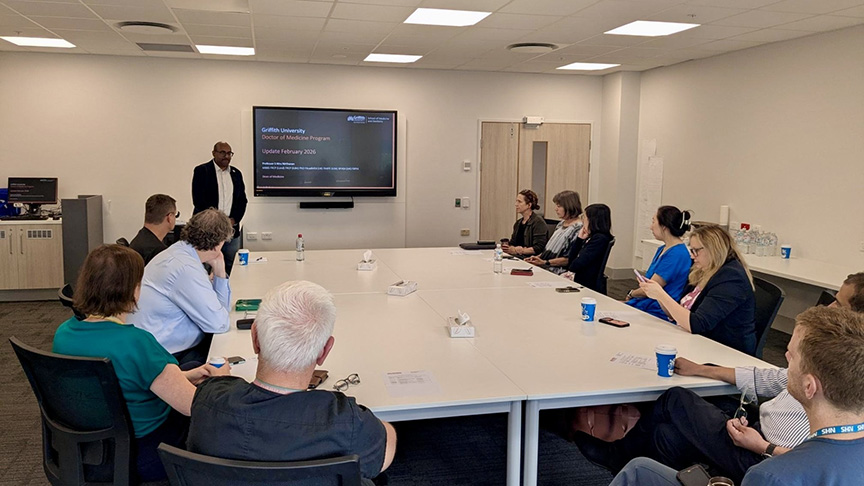 A group of diverse individuals seated around a conference table engaged in discussion in a well-lit meeting room.