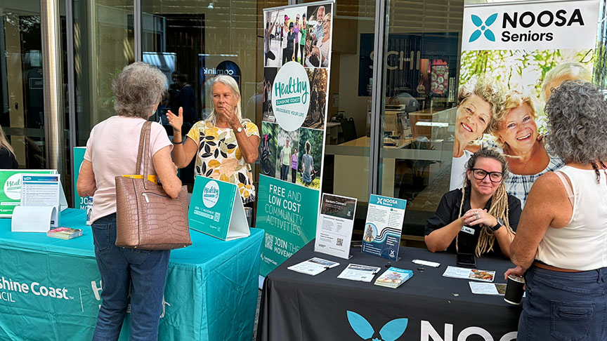  A participant at the Healthy Ageing Forum stands at the Noosa Seniors Centre stand, engaging with attendees.